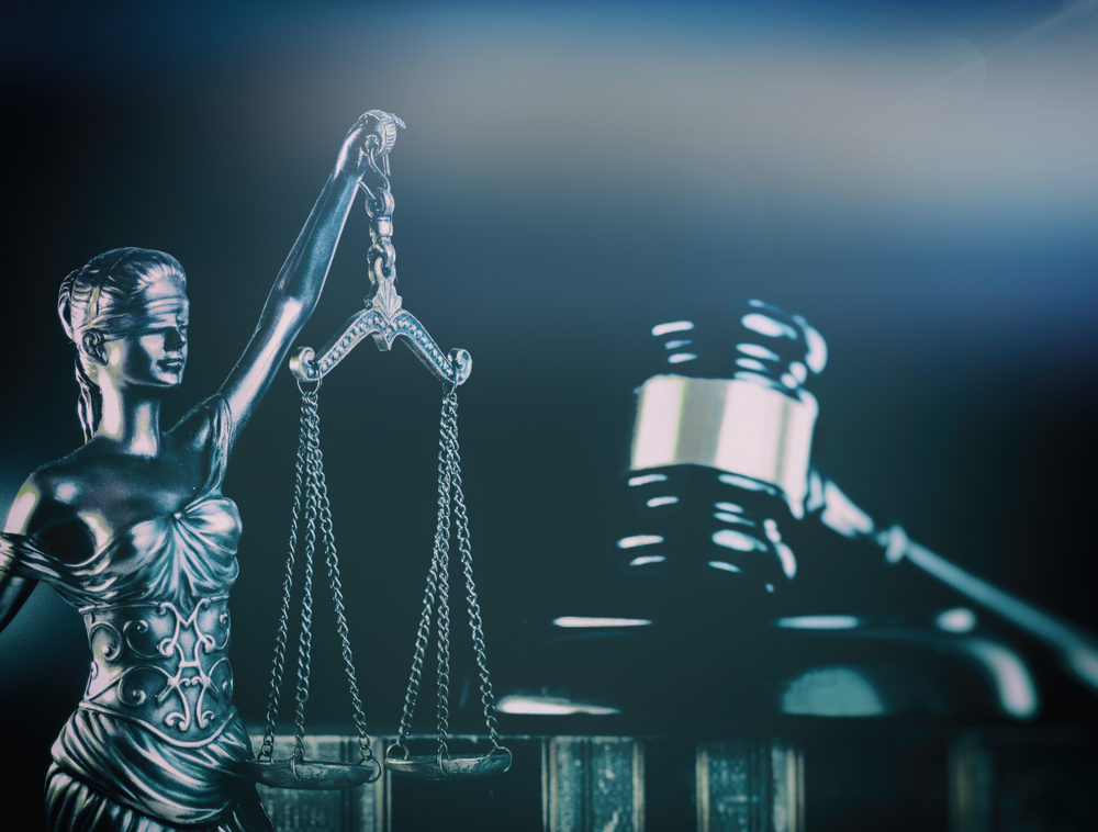 The scales of justice and a gavel in a navy blue rendering