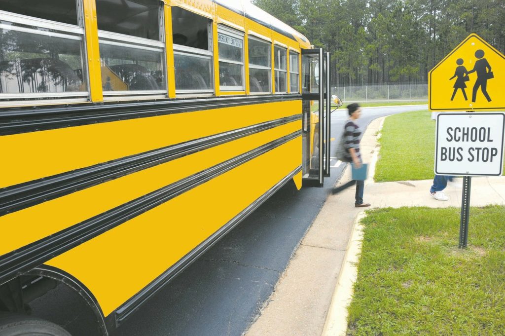 Students hop off a yellow school bus at a school bus stop