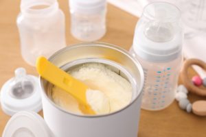 Can of powdered infant formula with scoop on table, closeup.