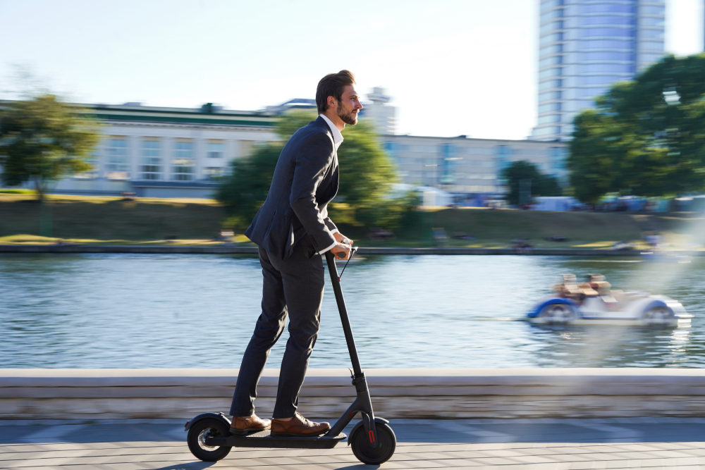 Businessman in a suit riding an e-scooter past a riverway