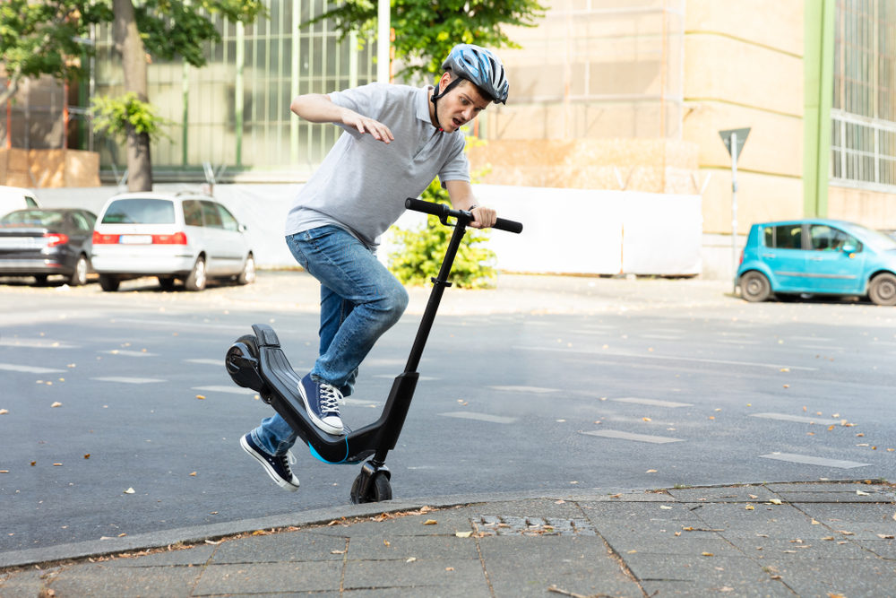 A scooter rider falling towards the pavement after hitting a curb