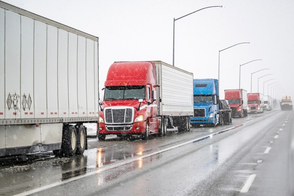 semi trucks with trailers transporting commercial cargo moving cautiously on a slippery highway during a winter snow