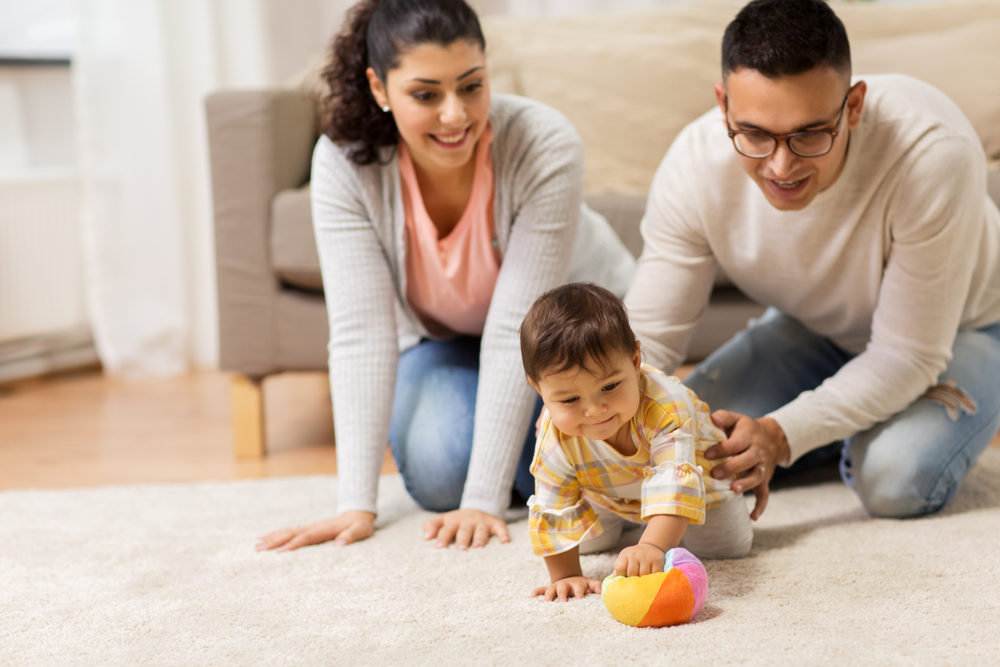 Young father, mother, and baby girl playing with a ball at home