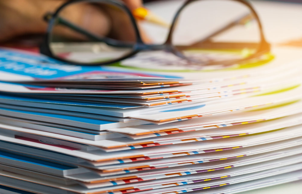 A pair of glasses sits atop a large pile of file folders