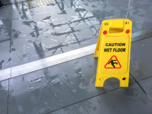 A yellow sign reading CAUTION WET FLOOR on a slippery looking wet floor
