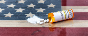 White pills spilling from a prescription bottle on to a United States flag