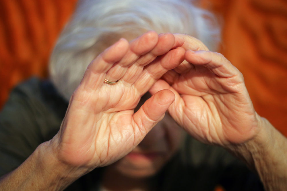 An elderly lady holds her hands in front of her face for protection