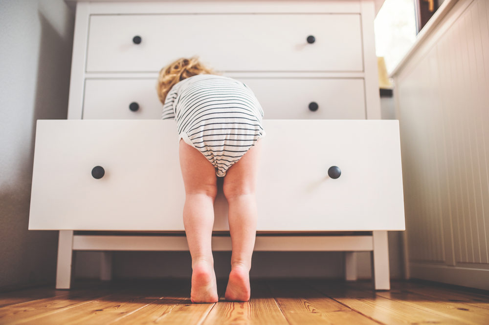 A toddler stands on his toes to reach into a dresser drawer