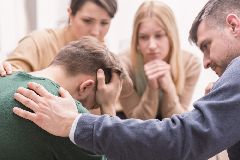 A group of people supporting a man with his head in his hands