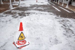 An orange cone warns of slippery conditions on a snow covered walkway