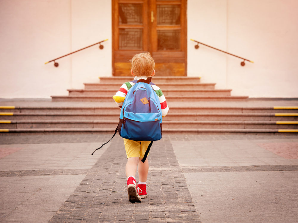 A young boy wearing a backpack approaches school doors