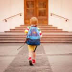 A young boy wearing a backpack approaches school doors