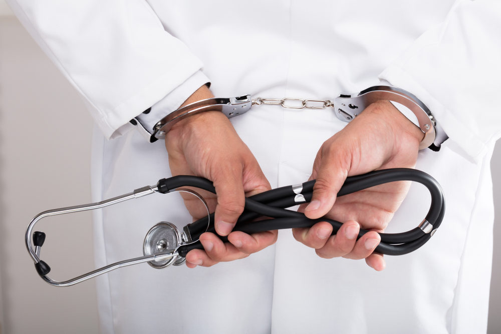A doctor's hands are in cuffs while still holding a stethoscope