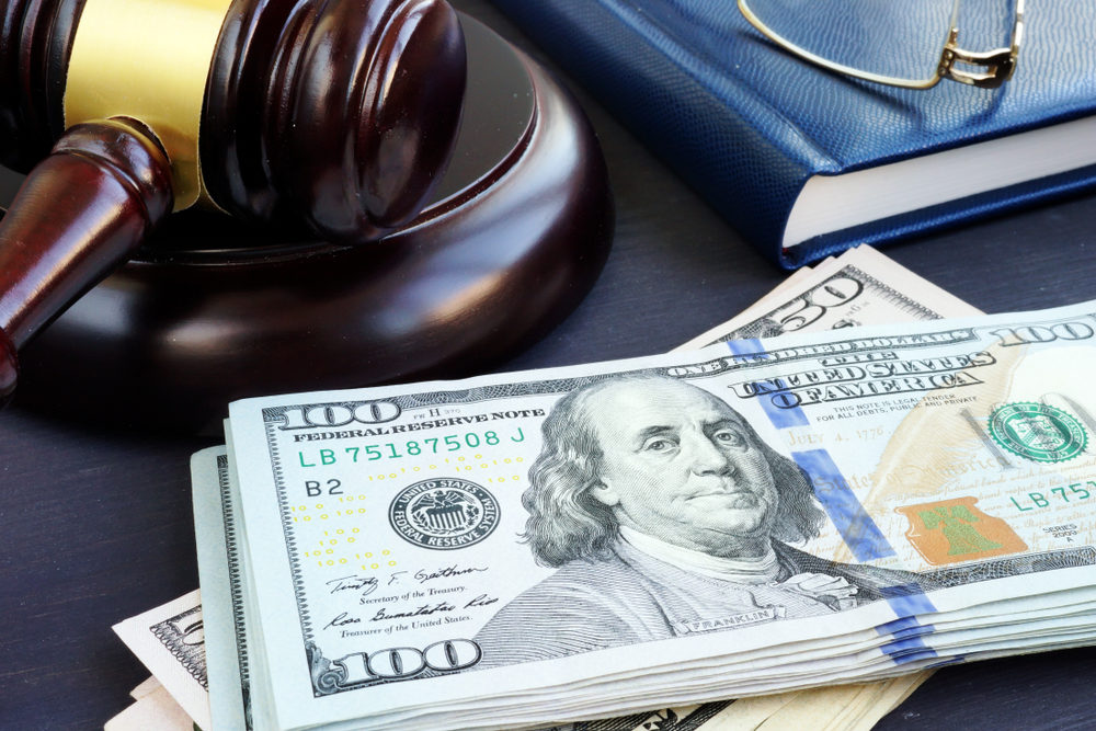 A stack of $100 and $50 bills sits beside a gavel on a desk