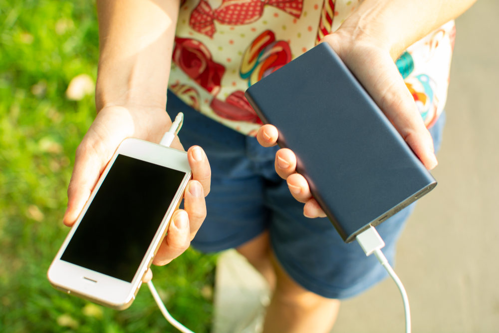 A woman holds out a black powerbank connected to a white phone