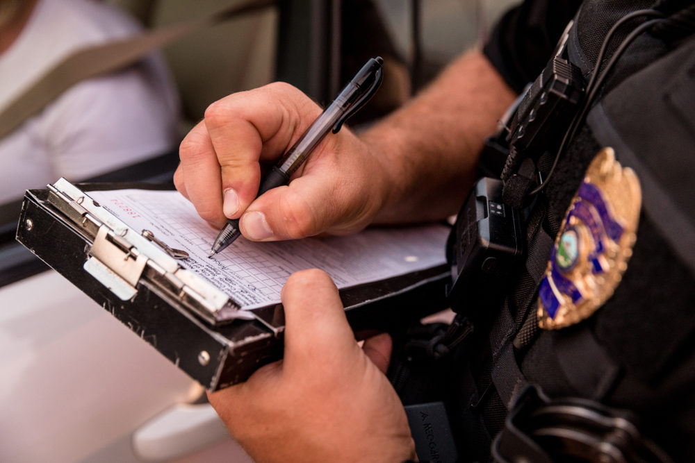 A police officer writes out a ticket beside a pulled over vehicle