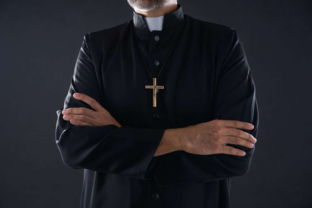 A senior priest with his arms crossed. 