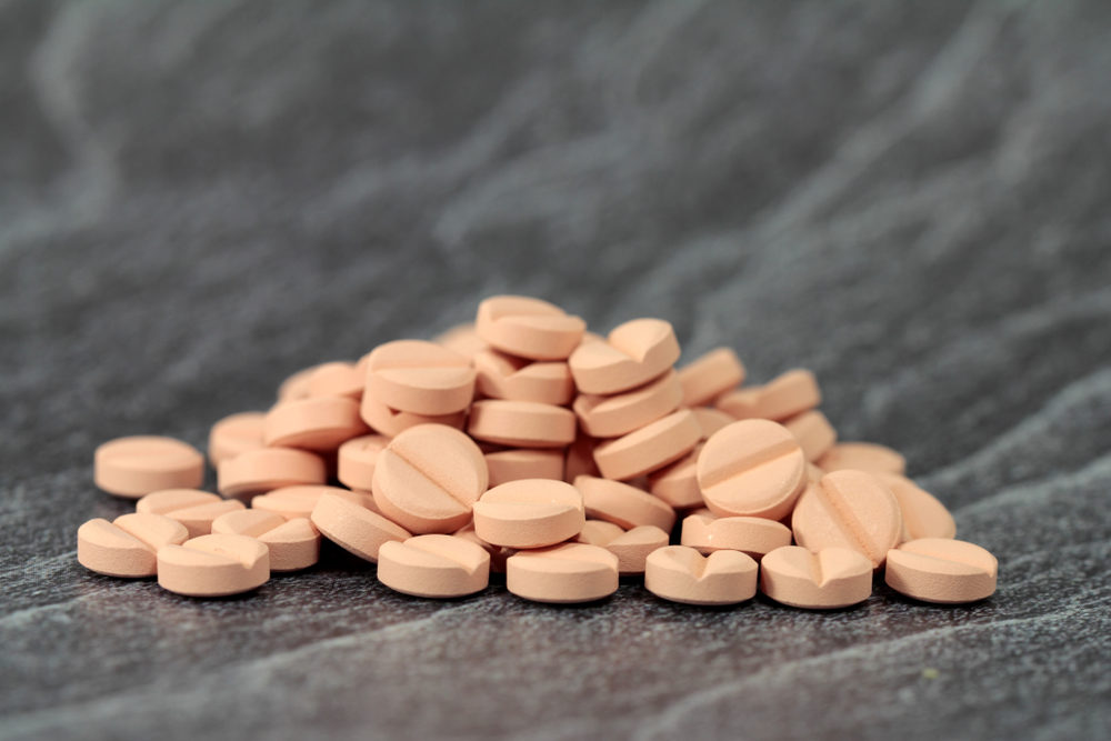 A pile of orange pills on a dark marble countertop