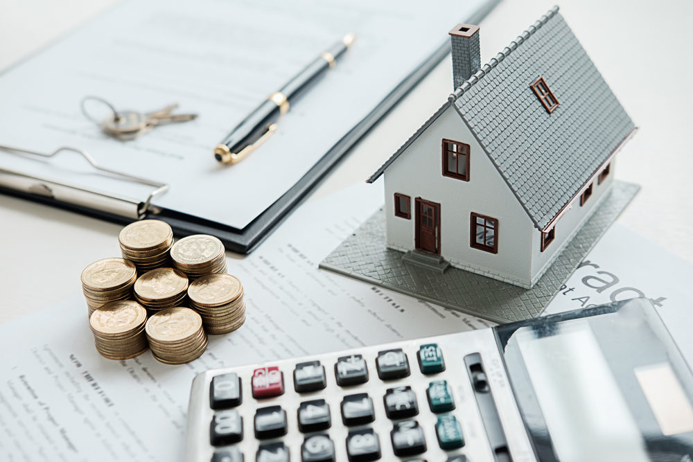 [Concept Art] small model of a home with coins, a calculator, and documents