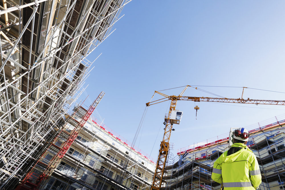 A surveyor glances up at a large crane and construction project