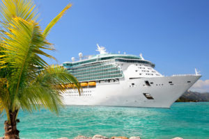 A large luxury cruise ship sails past a palm tree in turquoise blue waters