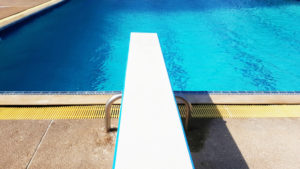 A white springboard hangs over an empty swimming pool