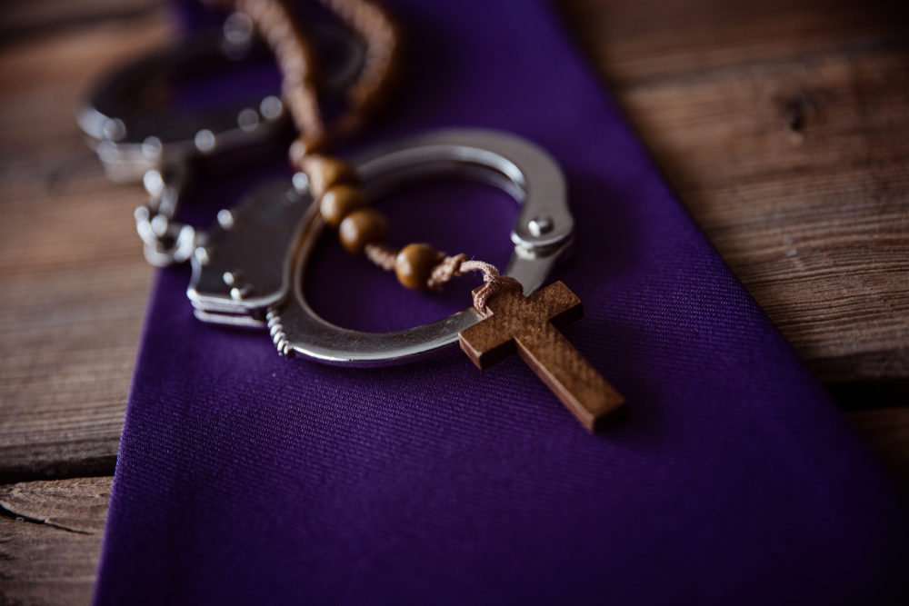 Wooden rosary draped across a pair of handcuffs