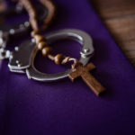 Wooden rosary draped across a pair of handcuffs
