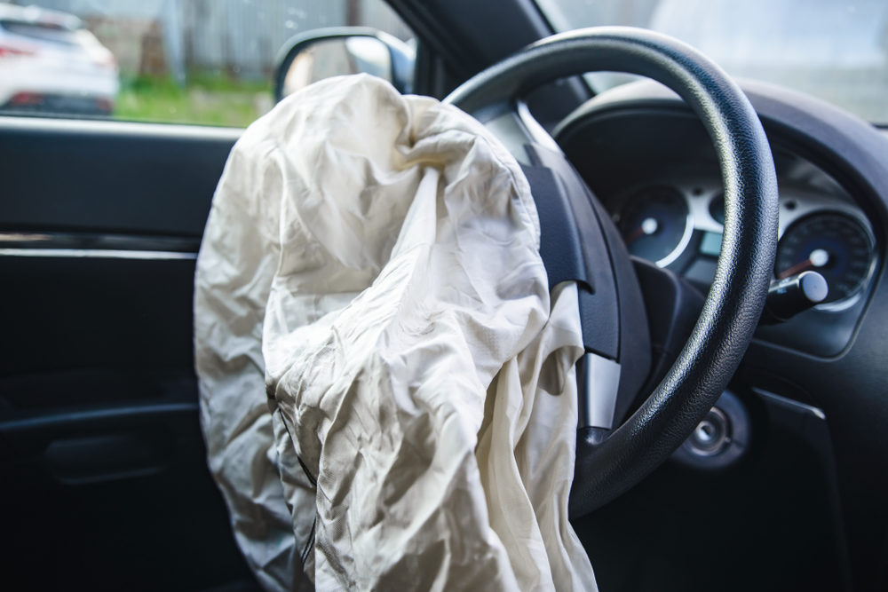A deployed airbag hangs from the steering wheel inside a car