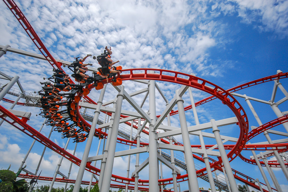 A rollercoaster train whips through the corkscrew section of a red roller coaster
