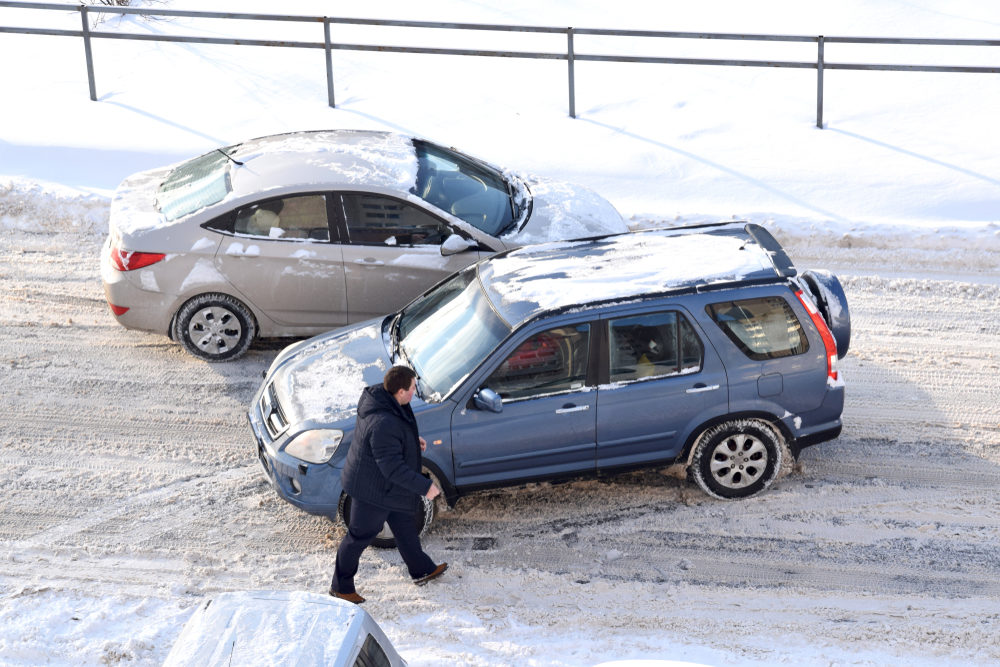 A man inspects the damage after two vehicles collide on a snowy road