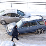A man inspects the damage after two vehicles collide on a snowy road