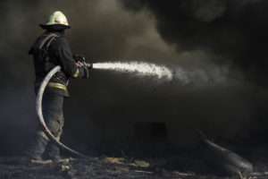 A firefighter spraying a hose into a thick cloud of black smoke