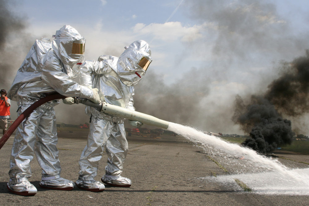 EPA Updates Information on PFAS as Parents File Firefighting Foam Lawsuit Two firefighters in protective suits spraying chemicals at an airport with smoke in the background