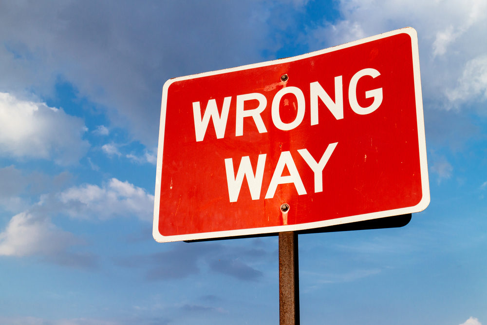 A red "Wrong Way" road sign against a cloudy sky