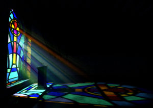 A stained-glass window casts a light upon an altar inside a dark church