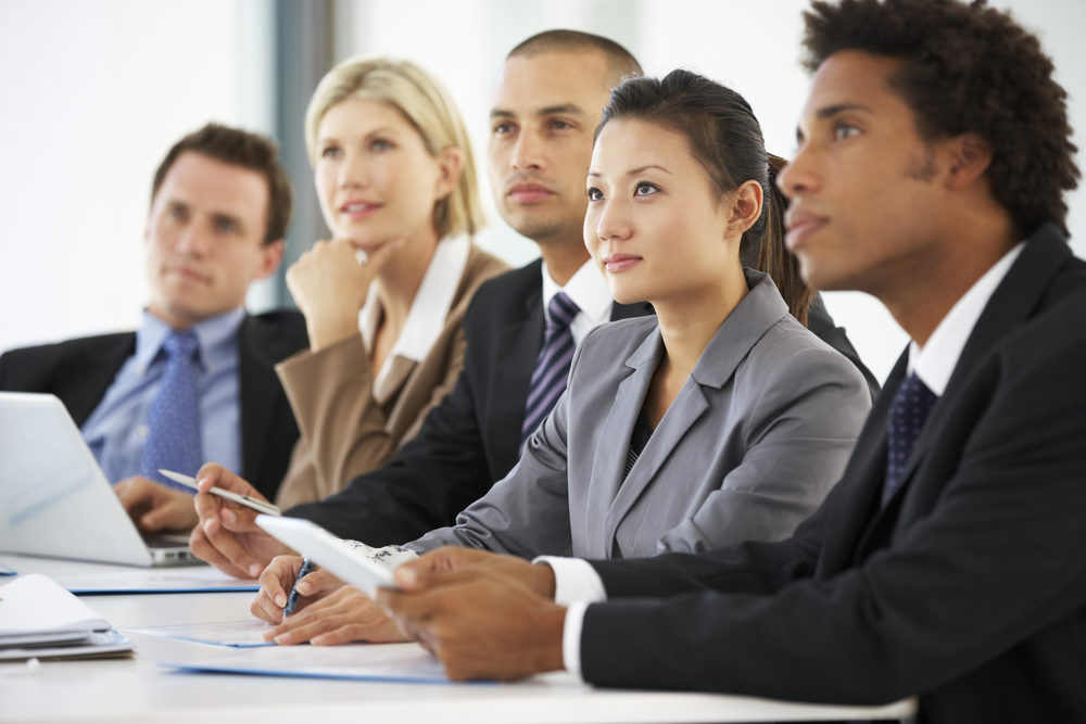 A group of people of various races sit at a conference table