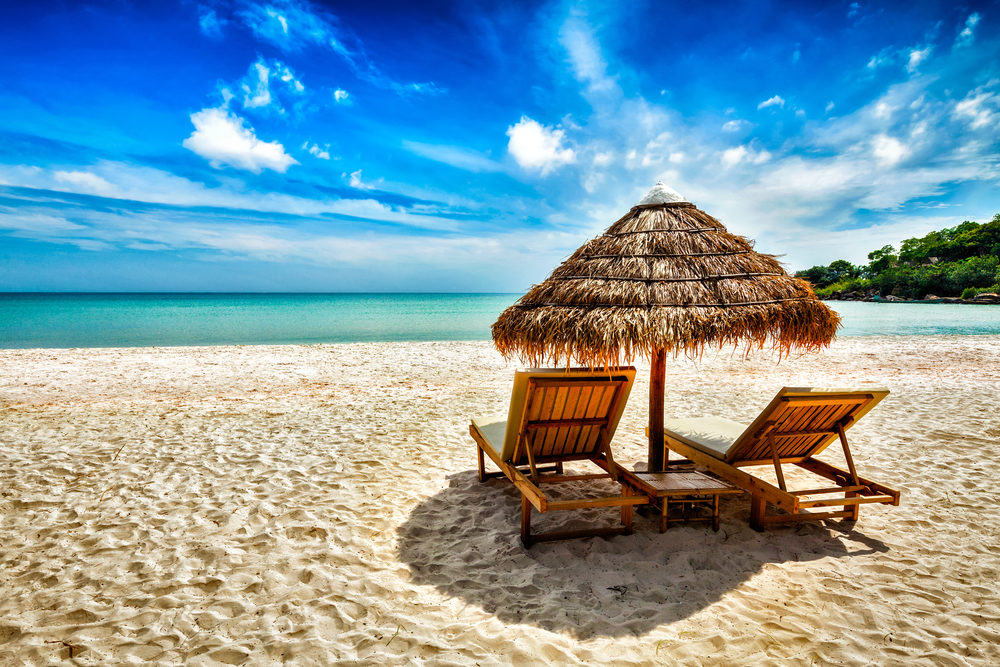 Two empty beach chairs under a grass umbrella