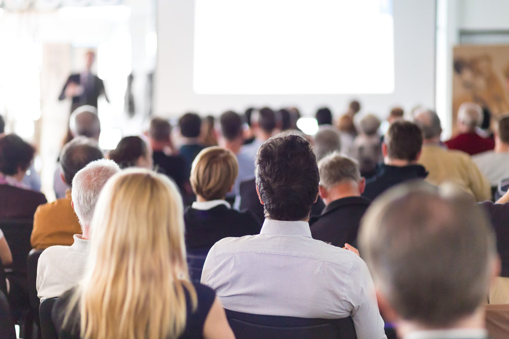 A speaker gives a talk in front of a room full of people