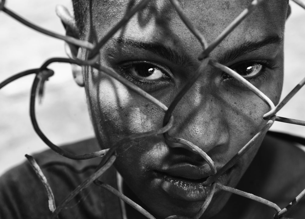 An African American woman stares through a chain-link fence