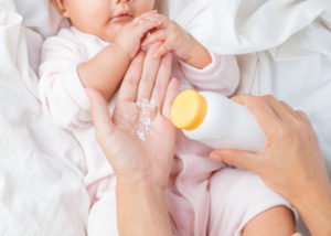 A mother holding baby powder above an infant