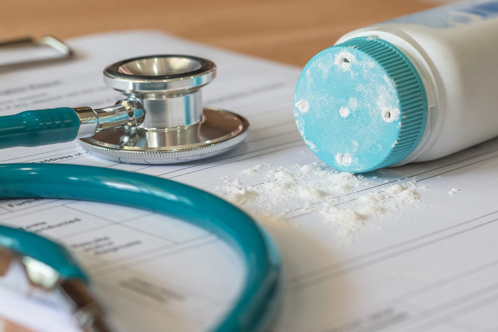 A bottle of baby powder spills onto a medical form with a stethoscope laying on it