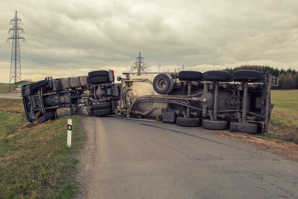 A large truck lies on it's side on a rural road after wrecking
