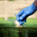 A gloved hand takes a water sample in a test tube