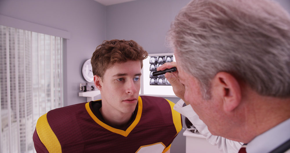 A doctor shines a flashlight in a male teenage football player's eye 