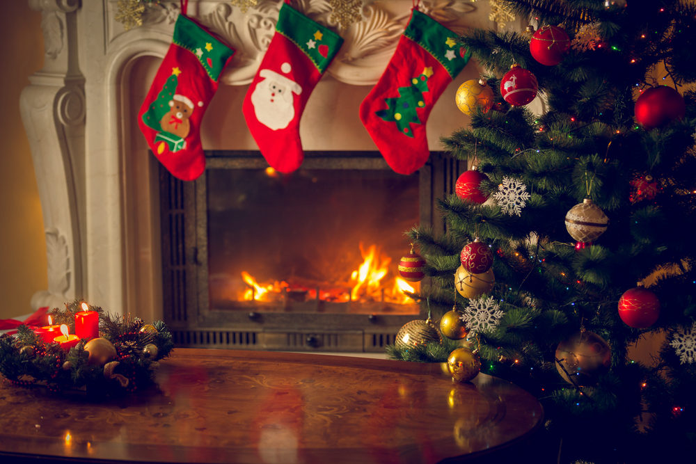 Stockings hung over a burning fireplace with a Christmas tree in the foregroiund