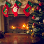 Stockings hung over a burning fireplace with a Christmas tree in the foregroiund