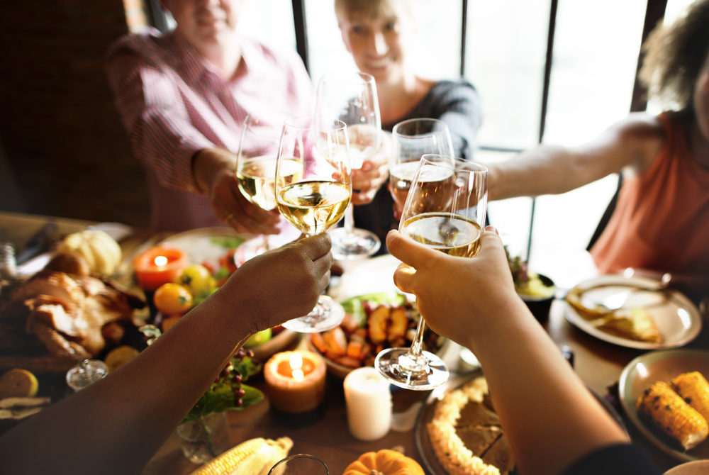 People clinking wine glasses over a Thanksgiving feast