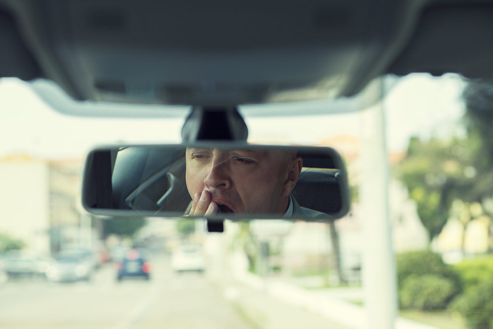 A male driver seen yawning in his rearview mirror