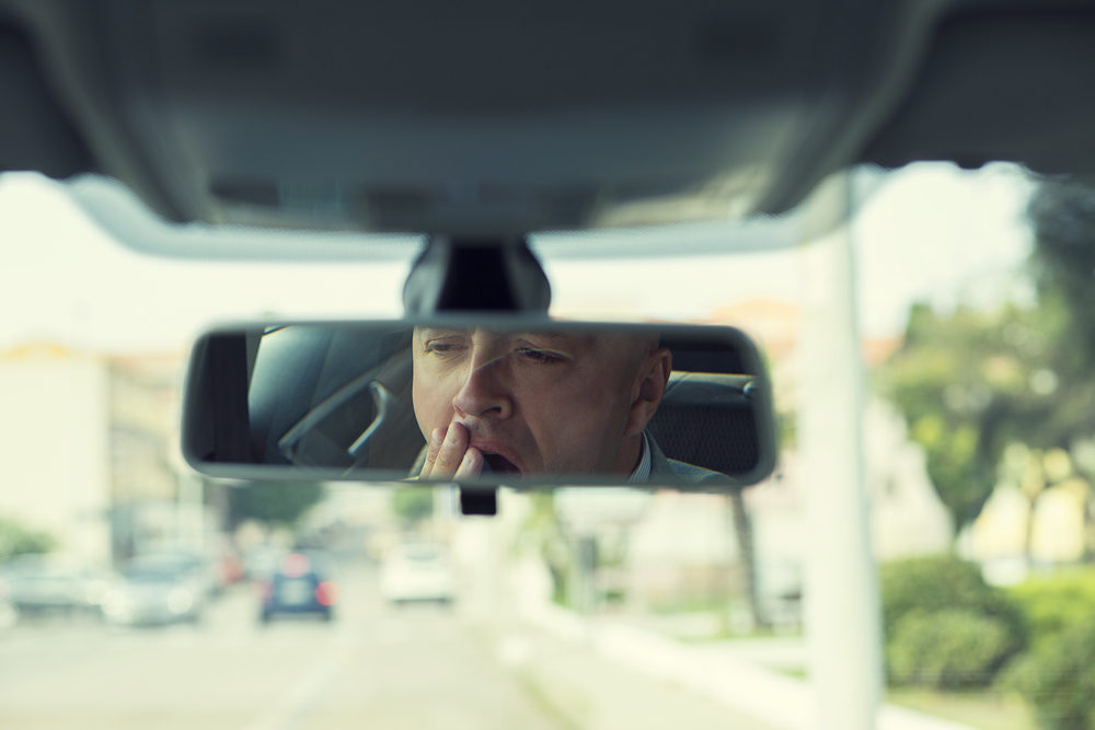 Drowsiness and the Older Driver A male driver seen yawning in his rearview mirror